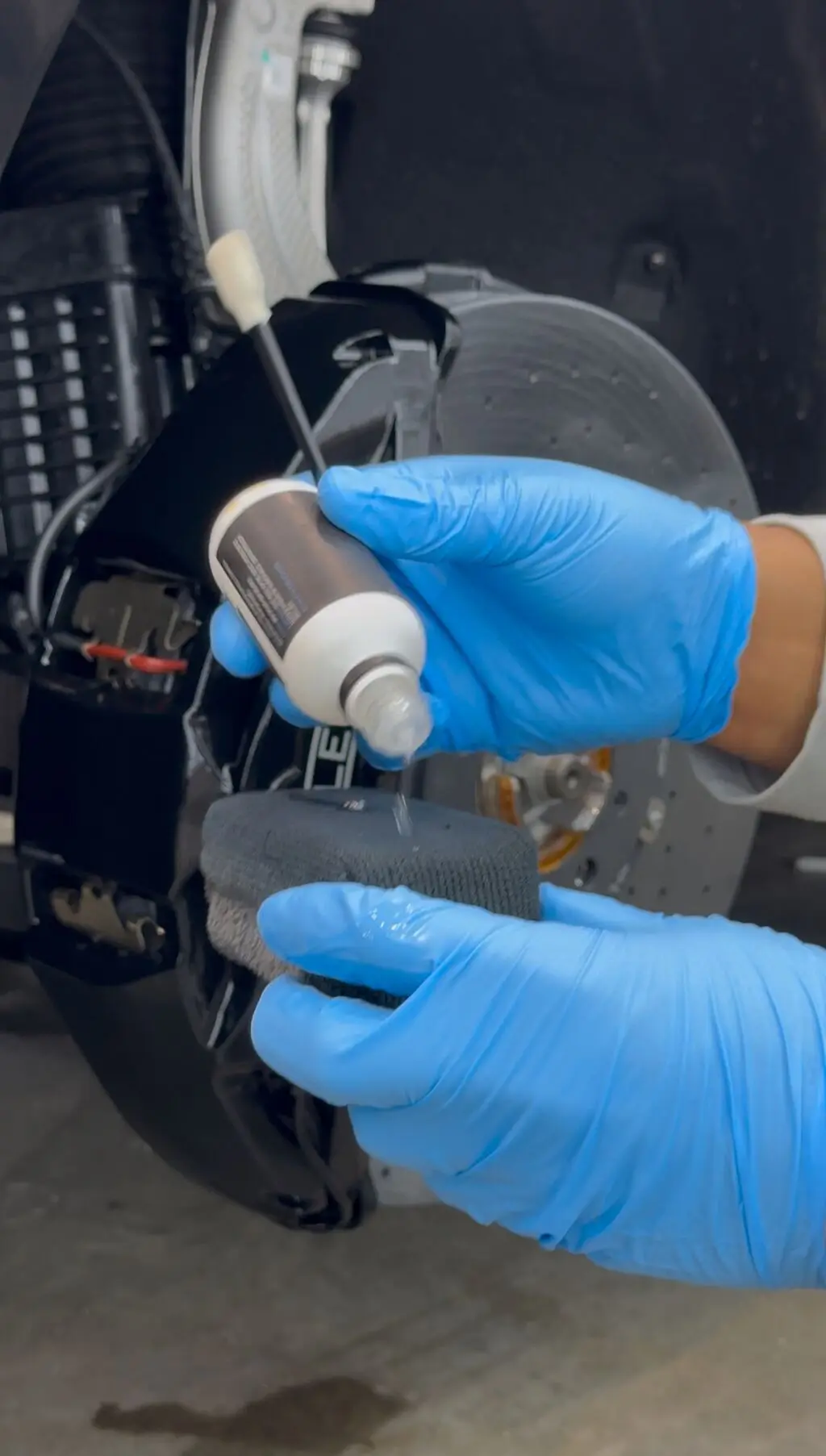 Gloved hands hand-applying a high temperature ceramic coating to a red brake caliper during a wheel-off detail at Secret Touch Auto Spa in Shrewsbury MA